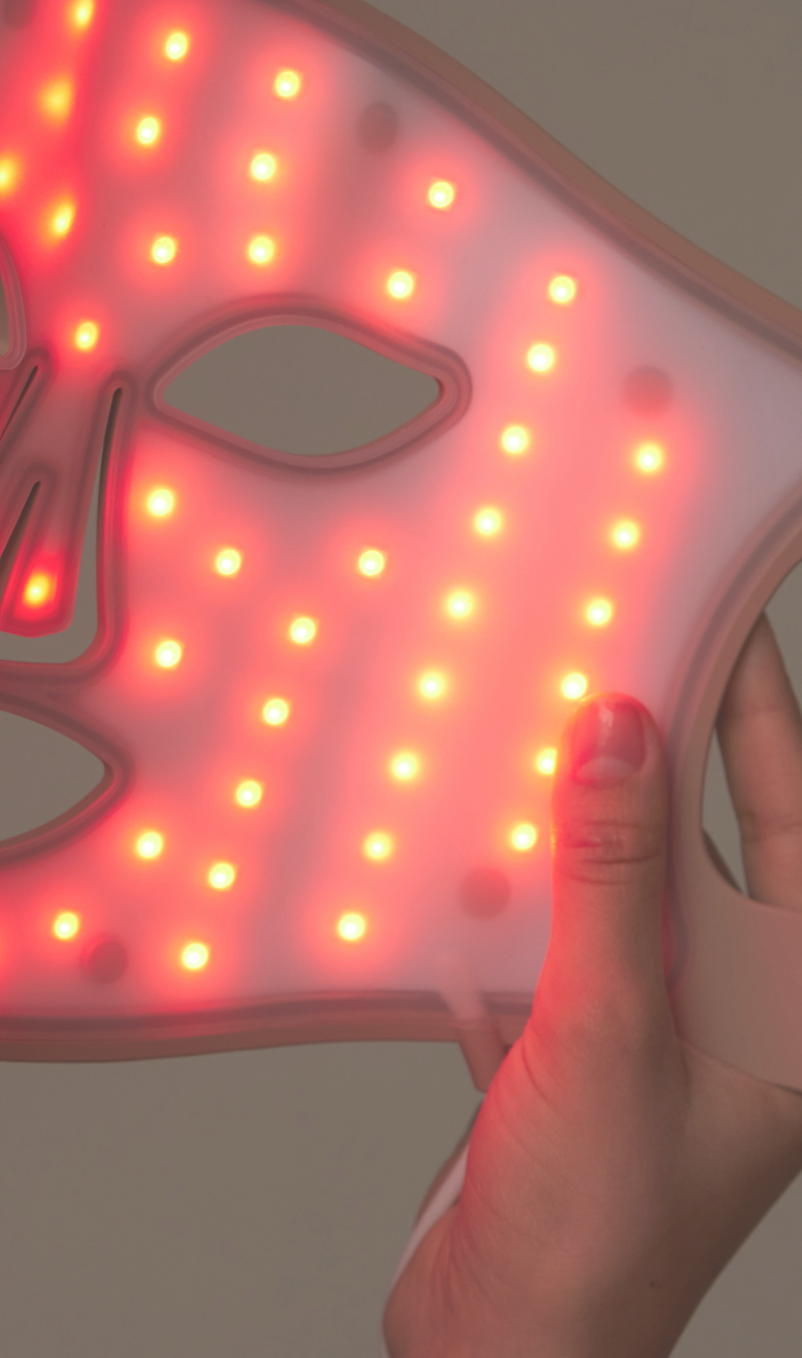LED face mask with red light held by a hand against a neutral background
